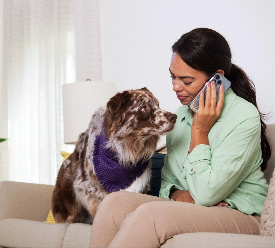 Woman on the phone with a dog sitting next to her on a couch.