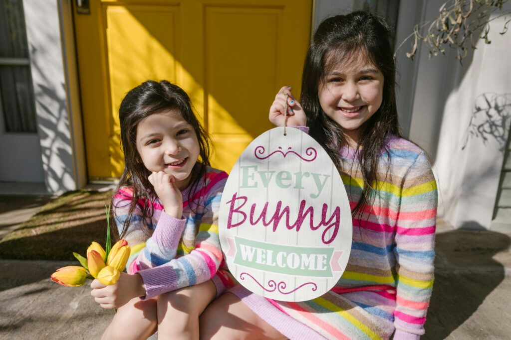 Two girls smile while one holds flowers and the other holds an Easter sign