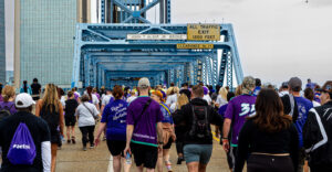A large crowd of people walk across a blue bridge