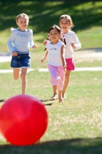 Three children run toward a red ball in a field
