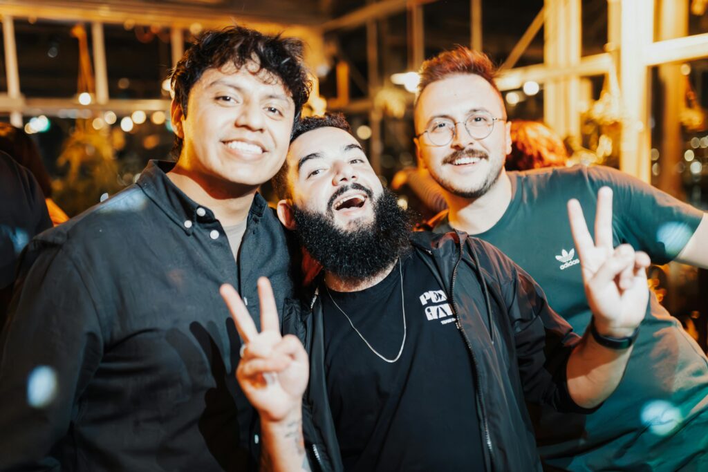 Three men smile and one holds up peace signs