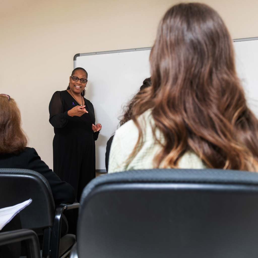 A woman stands at the front of a room while speaking in front of a crowd